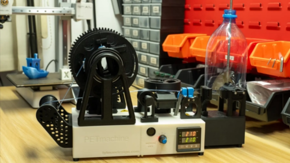 A filament extruder is shown on a workbench. On the front is a knob and the display of a PID controller. A black geared spool is mounted on the top of the extruder, and on the right, a clear plastic bottle is positioned over a metal rod.